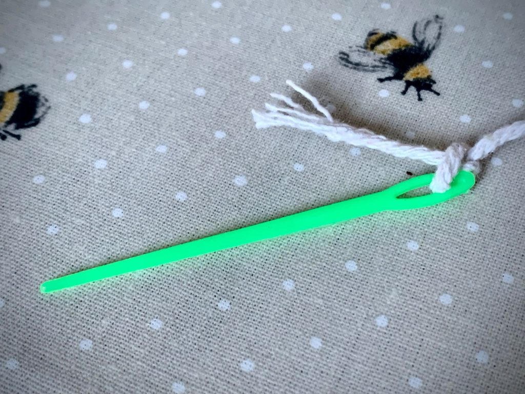 Small green plastic sewing needle for making a woodland necklace.